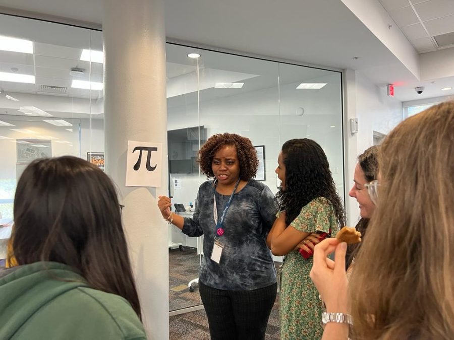 Faculty and students gather around a picture of pie, a mathematical symbol. Before the discussion, groups talked about a certain symbol taped to the wall and discussed their meanings and connotations. Other symbols discussed included a piñata, the Nike swoosh, and a swastika.