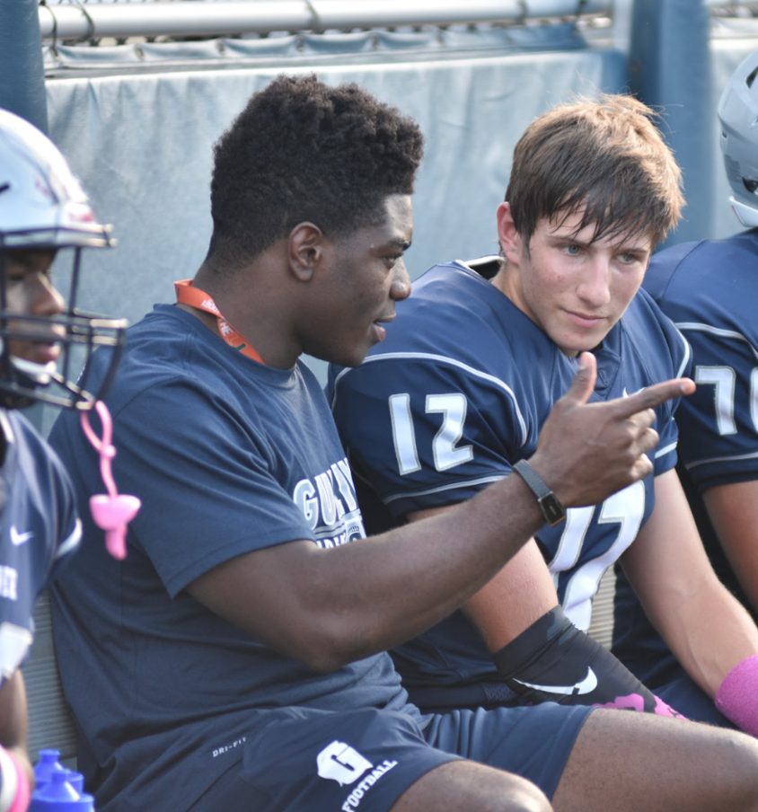 Robert Burns talks with quarterback Will Poses during the Homecoming Game in 2016 against Monsignor Pace. Burns sat out this game, but gave his teammates advice from the bench. Although the team lost, they were enthusiastic to play their homecoming game on home turf.