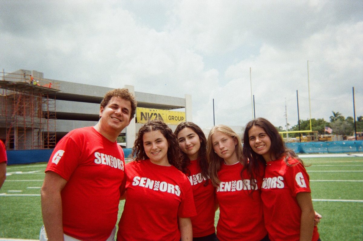 A group of seniors smile on the Sean Taylor 01 Memorial Field before taking the senior class picture. The photo was taken on a disposable camera which senior Sara Gelrud has been using to document her final year of high school. I bring it to every special occasion. I love getting each roll developed and being surprised by some pictures I didnt even remember taking, she said.