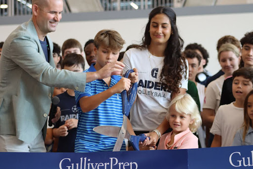 President Simon Hess hands the scissors to Freshmen Ari Candib and Junior Gabriela Fernandes. Students, from grades K-12, gathered around them as they cut the ribbon to the new Athletic Center.