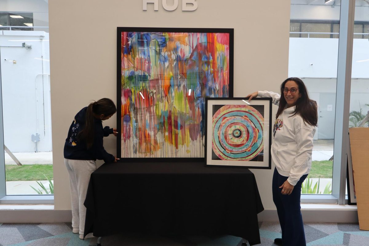 Stacey Goldman, Art Department Chair and alumna, sets up her art work for the alumni exhibit  at the Art Walk Festival along sophomore Sophia Gonzalez. The alumni exhibit will take place in the Upper School New Academic building. The festival will be opened to the public from 9 a.m. to 4 p.m.