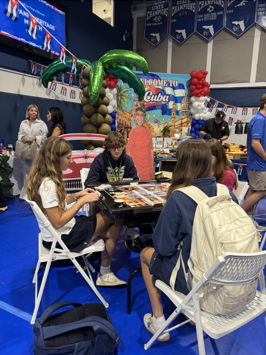 Students gather at the Cuba booth, which featured traditional food like croquetas, dominoes, and colorful decorations. The booth was decorated with a palm tree balloon display and a cutout of Cuban singer Celia Cruz. Students enjoyed learning about Cuban culture while sampling food and playing games.
