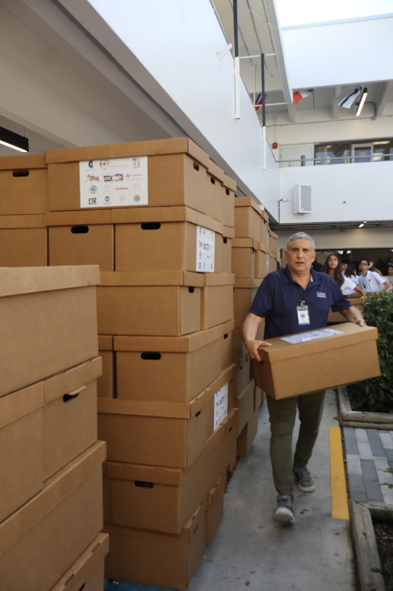 Mr. Gisonni lifts one of the packed Thanksgiving boxes as volunteers continue assembling the remaining stacks beside him. These boxes make up the full Thanksgiving meals that will be delivered on Nov. 25 to families served by the Overtown Youth Center.