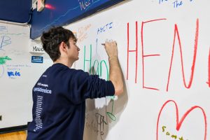 Junior Chase Samole signs the Blue Dungeon wall during the “Goodbye Blue Dungeon” open house on May 9. Students, alumni, parents and faculty filled the gym one final time to leave messages and reflect on the memories created inside the historic space before its replacement by the new STEM Commons Building.
